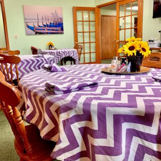 A cozy dining room with tables covered in purple zigzag patterned tablecloths, adorned with a vase of sunflowers.
