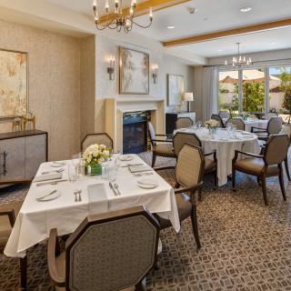 An elegant dining room with neatly arranged tables and upholstered chairs, featuring a chandelier and sophisticated decor.