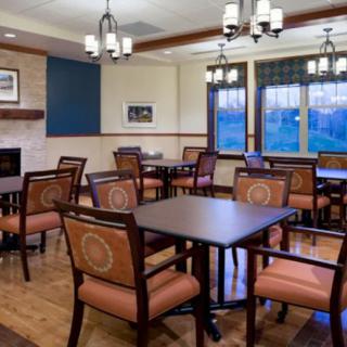 A cozy dining area with wooden tables and upholstered chairs, featuring elegant lighting and large windows.