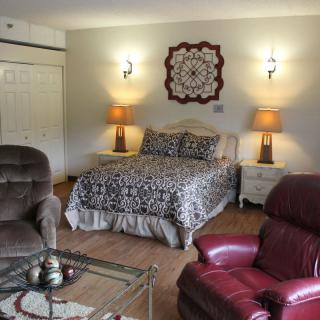 Cozy bedroom with a bed, armchairs, and warm lighting.