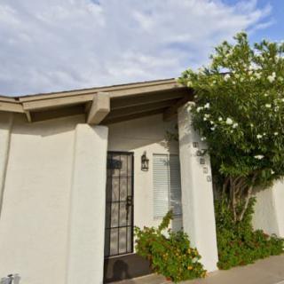 A small house entrance with a metal gate and surrounding greenery on a sunny day.