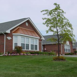 A suburban brick house with a well-maintained lawn and young tree.