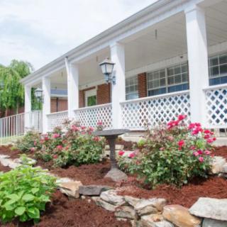 A charming house with a beautifully landscaped garden featuring roses and a spacious porch.