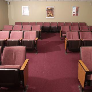 An empty theater room with rows of maroon seats.
