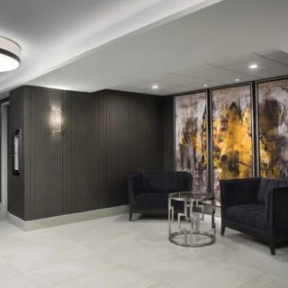 A modern lobby area featuring dark chairs, a decorative wall with artwork, and ambient lighting.