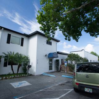 A white building with a parked car and trees under a blue sky.
