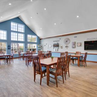A spacious dining area with wooden tables and chairs, large windows, and bright lighting.