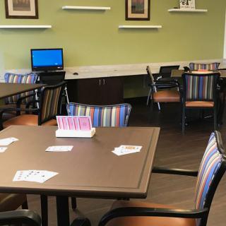 A cozy room with tables, chairs, a computer station, and scattered playing cards.