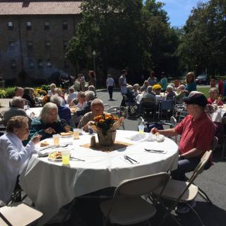 A group of people enjoying an outdoor gathering on a sunny day, seated around tables.