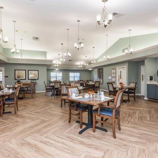 A spacious dining room with neatly arranged tables and chairs, featuring elegant lighting and wood flooring.