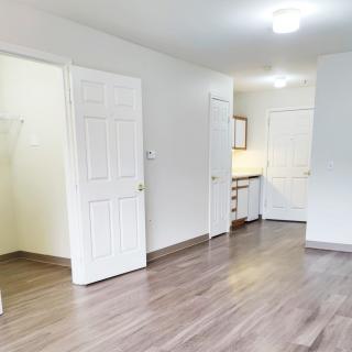 An empty room with wood flooring, open doors, and bright lighting.
