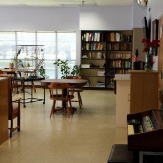 A serene library space featuring wooden tables, a wall of bookshelves, and indoor plants.