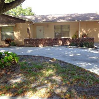 A single-story house with a driveway and front yard shaded by a large tree.