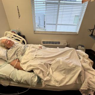 A patient resting in a hospital room, surrounded by medical equipment and natural light from a nearby window.