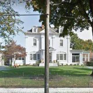 A white residential house with a well-kept lawn and surrounding trees.