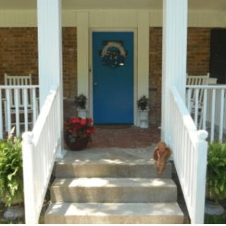 A welcoming front porch with a blue door, rocking chairs, and decorative plants.