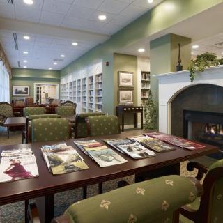 A cozy library interior with bookshelves, a fireplace, and a seating area for reading magazines.