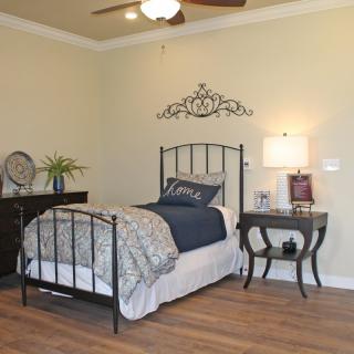 A cozy bedroom with a single metal frame bed, a nightstand with a lamp, and decorative wall art.