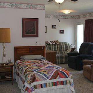 A cozy bedroom featuring a single bed with a colorful quilt, recliner, and sofa.