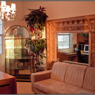A cozy living room with a sofa, large mirror, indoor plant, and elegant chandelier.