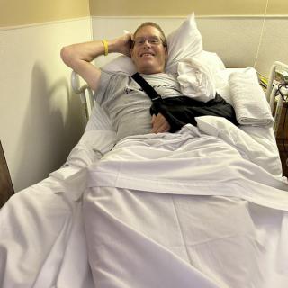 A patient resting in a hospital bed with an arm in a sling.