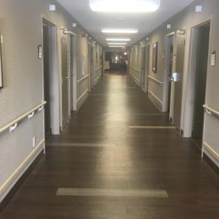 A well-lit hallway showcasing rooms with doors on either side, featuring a wooden floor and artwork on the walls.