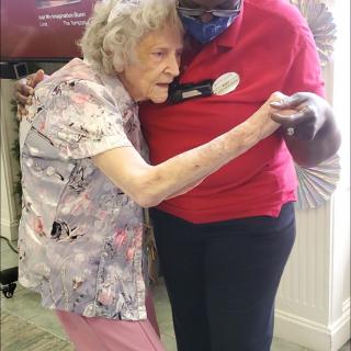 An elderly woman and a caregiver share a comforting embrace in a supportive environment.