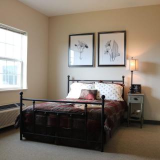 A cozy bedroom featuring a metal-framed bed with decorative pillows, framed artwork on the wall, and a bedside table with a lamp.