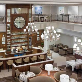 A spacious and elegant restaurant interior featuring a large clock, chandeliers, a bar counter, and comfortable seating areas.