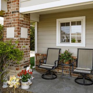 A cozy front porch with two chairs, a brick pillar, and decorative plants.