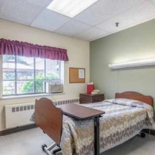 A hospital room with a single bed next to a window with curtains and an air conditioner.