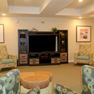 A cozy living room featuring a large TV, comfortable chairs, and decorative shelves.