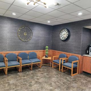 A cozy waiting area featuring wooden chairs and two decorative clocks.
