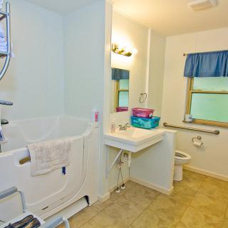 An accessible bathroom featuring a walk-in bathtub, sink, and toilet with grab bars for support.