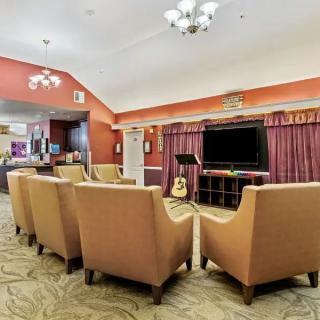 A cozy living room setup with several chairs facing a television, a guitar leaning against the TV stand, and elegant chandeliers hanging from the ceiling.