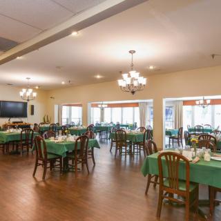 A spacious dining room with tables set and chandeliers hanging from the ceiling.