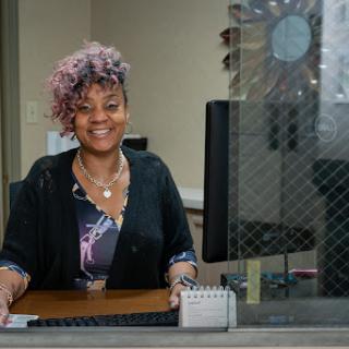 A cheerful woman at her desk in an office setting, ready to assist.