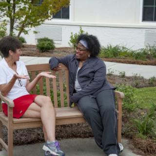 Two people having a friendly conversation on a bench outside.