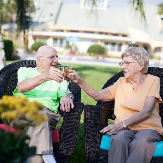 An elderly couple enjoying a drink together outdoors in a garden.