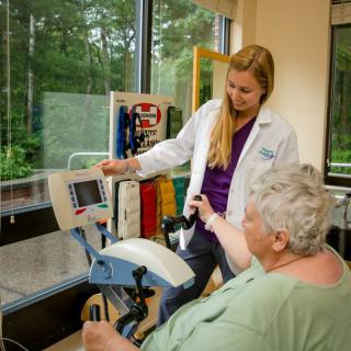 A healthcare professional assists a senior patient with physical therapy exercises using specialized equipment.
