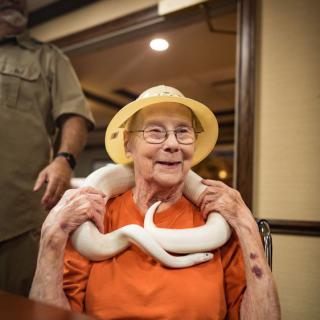 An elderly woman smiling with a white snake draped around her neck.