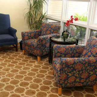 A cozy living room corner with floral patterned chairs, a small table holding an orchid, and a large window providing natural light.