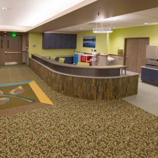 A modern lobby reception area with a curved desk, patterned carpet, and bright lighting.