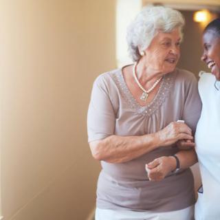 An elderly woman and her caregiver share a moment of laughter and support indoors.
