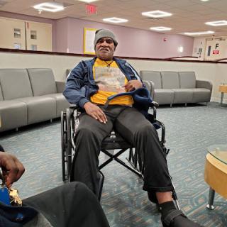 A person seated in a wheelchair in a hospital waiting area.