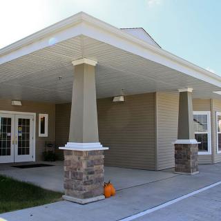 A building entrance with a covered area featuring columns and a pumpkin decoration on the ground.