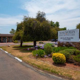 A view of a motel entrance with a sign, surrounded by landscaped greenery and trees.