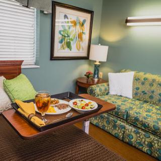 A cozy and inviting room featuring a comfortable sofa, a small dining table with a meal, and colorful artwork on the wall.