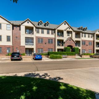 A suburban apartment building with a parking lot and cars in front.
