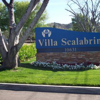 Entrance sign for Villa Scalabrini surrounded by trees and landscaping.